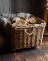 Wicker basket with logs inside on a wooden floor next to a fireplace.