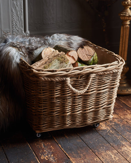 Wicker basket with logs inside on a wooden floor next to a fireplace.