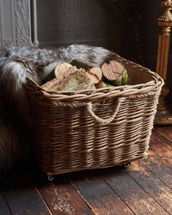 Wicker basket with logs inside on a wooden floor next to a fireplace.